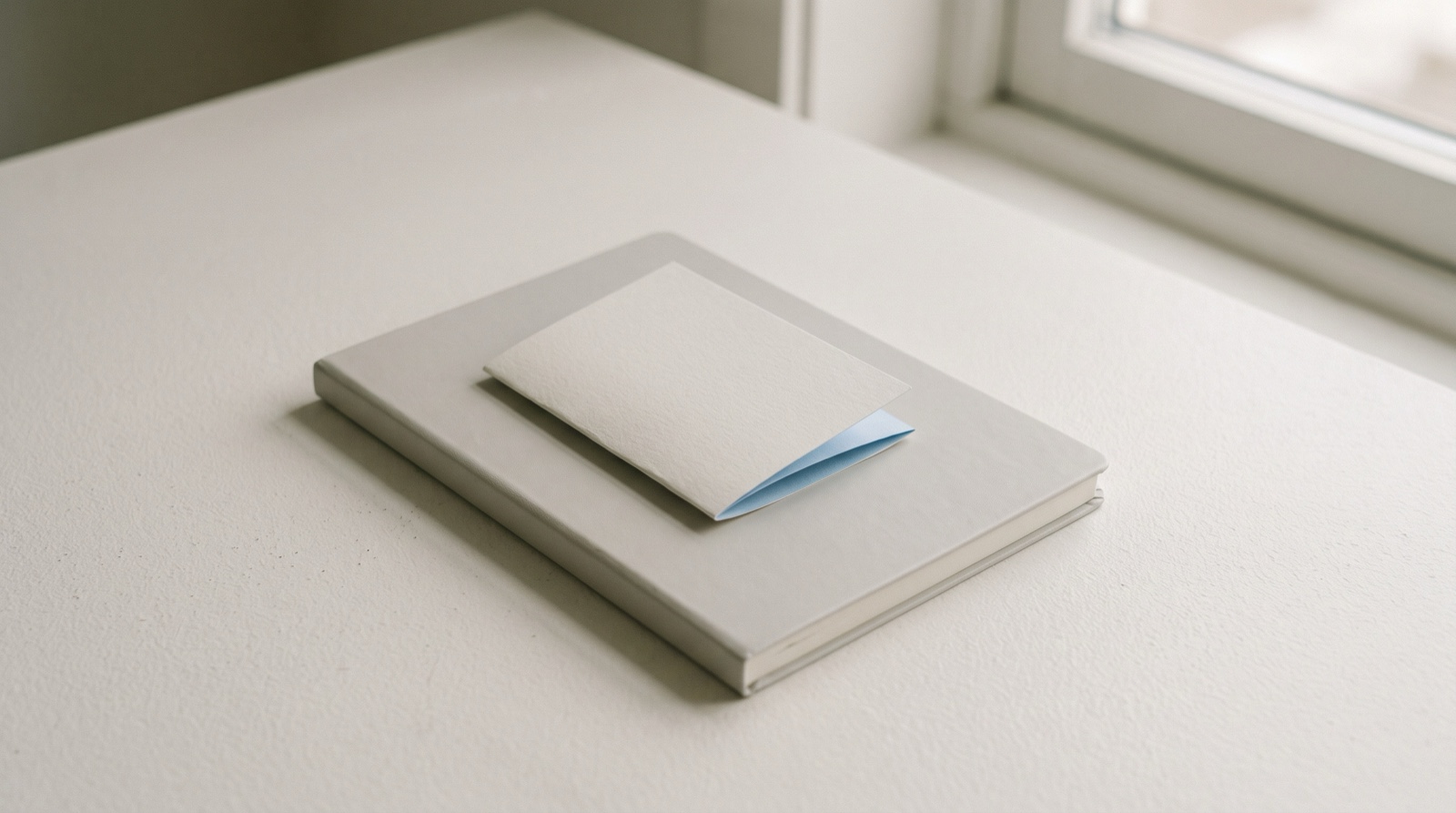 A small folded paper note with a sky-blue inner fold resting on a closed pale-grey notebook, like a short entry that counts as much as a full page.