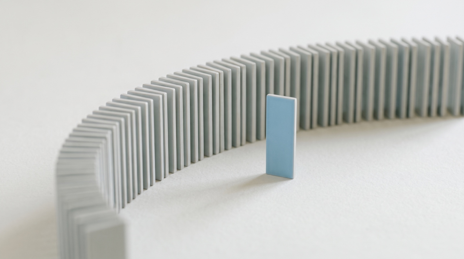 A long curved row of identical pale-grey tiles on an off-white surface, with one sky-blue tile stepped forward out of the row.