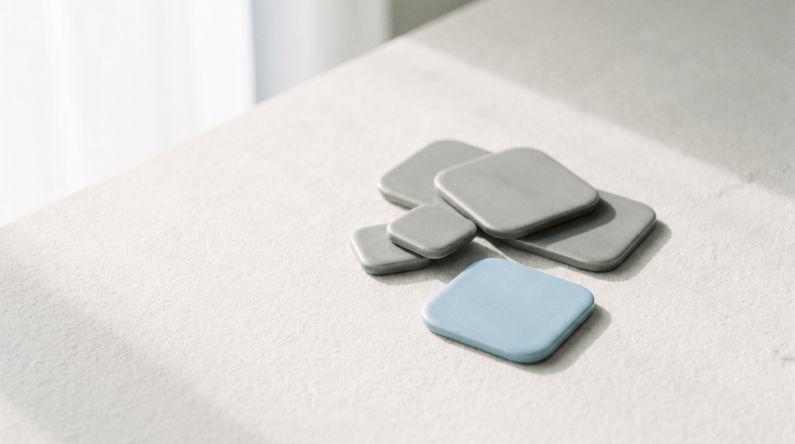A calm arrangement of soft rounded app tiles on an off-white surface, with one sky-blue tile standing slightly forward.