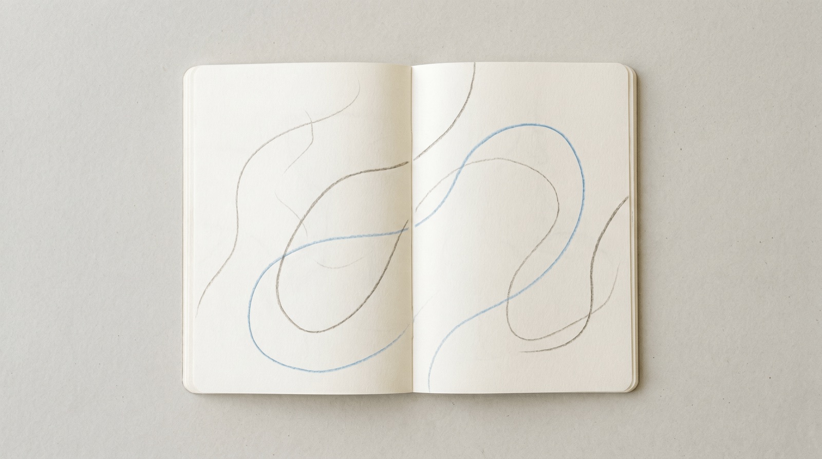 An open journal on a clean off-white surface, soft pale-grey strokes flowing loosely across both pages with one looping line in sky-blue, like thoughts emptied onto paper.