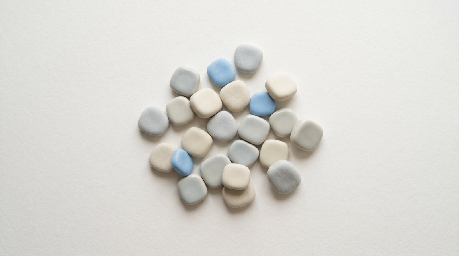 A loose cluster of soft rounded tiles in pale grey and sky-blue settling onto a clean surface, like thoughts emptied from a busy mind.