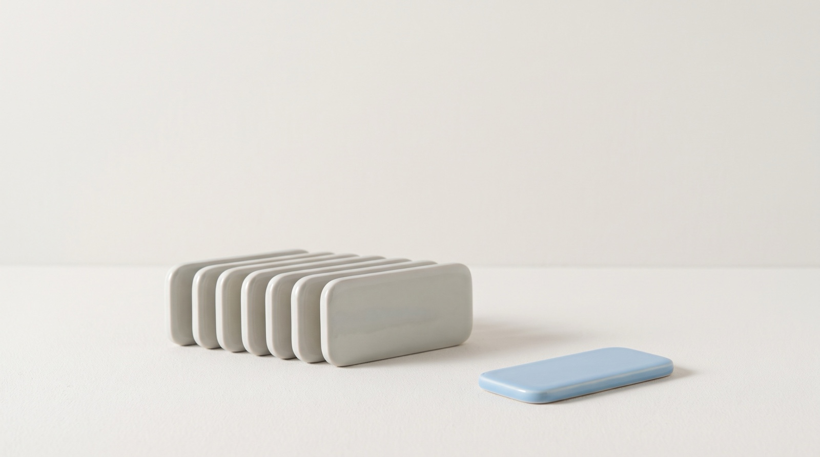 A neat row of pale-grey rounded tiles stacked together on a matte off-white surface, with one sky-blue tile set apart in front of them, like the day closed and tomorrow chosen.