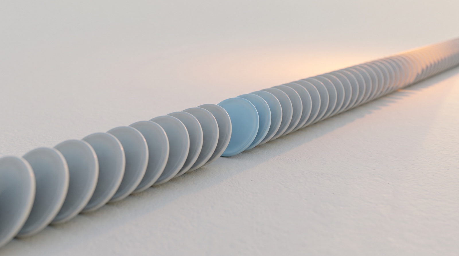 A repeating line of small pale-grey discs leaning gently onto each other across a calm off-white surface, one disc in sky-blue, with faint warm light at the far edge.