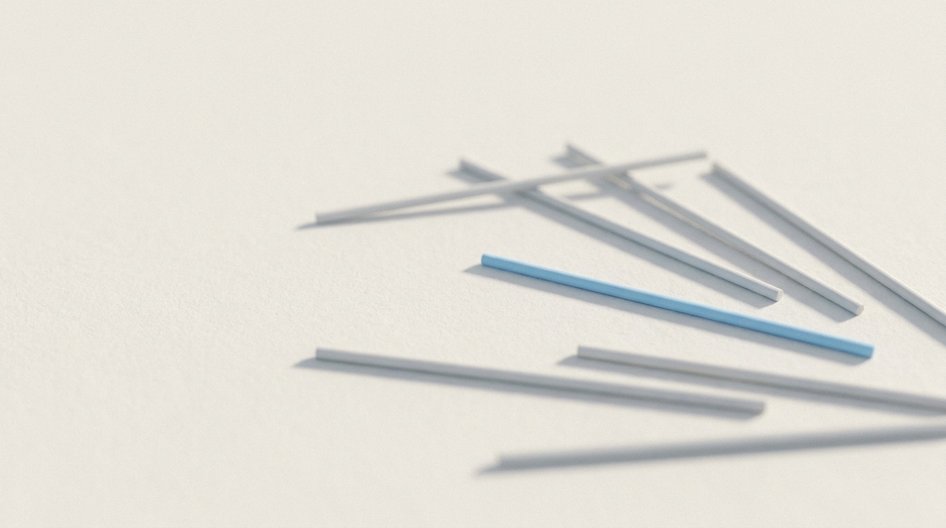 A scatter of soft-focus pale-grey rods on an off-white surface with a single sky-blue rod lying sharply in focus among them.