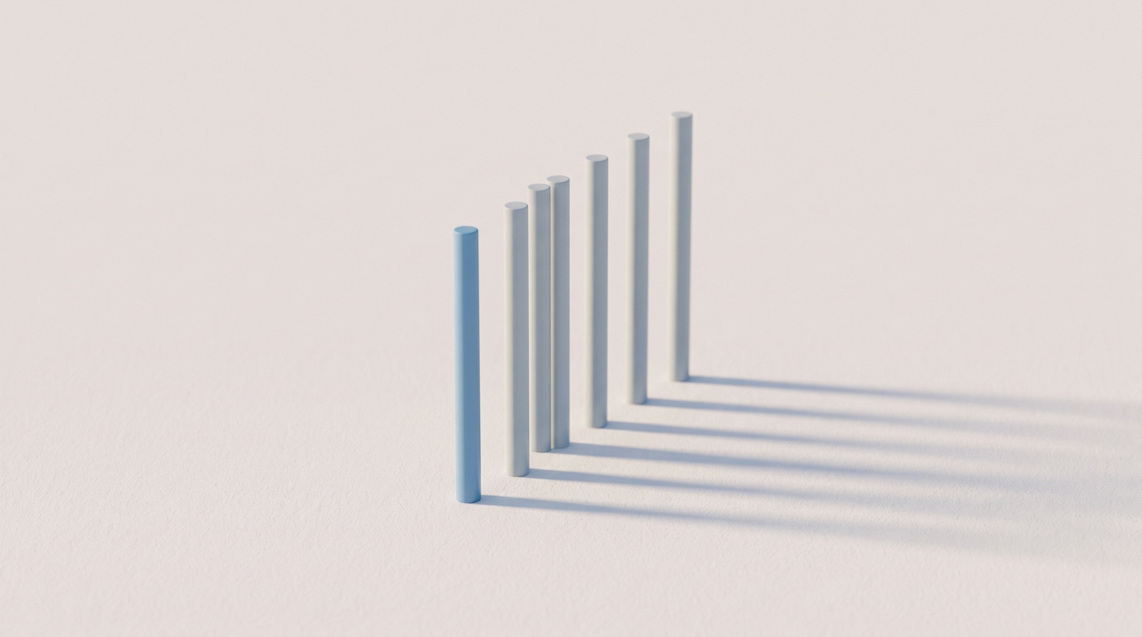 A line of slim pale-grey rods standing in order of height on a matte off-white surface, the nearest one sky-blue, casting long soft shadows in low end-of-day light, like a short ranked list waiting for tomorrow.