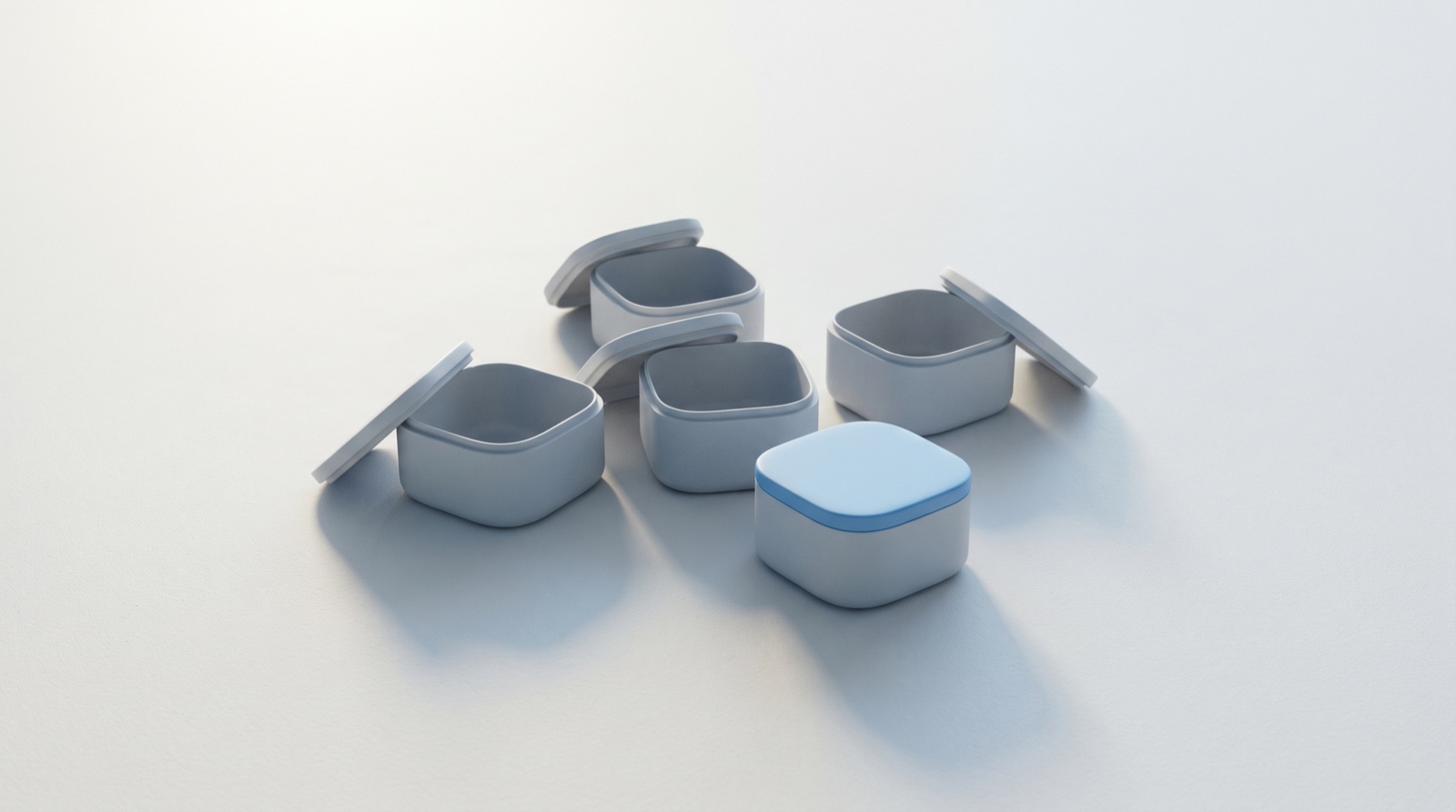 A small group of pale-grey boxes on a calm off-white surface, most with their lids lifted off and leaning beside them, and one box closed neatly with a sky-blue lid.