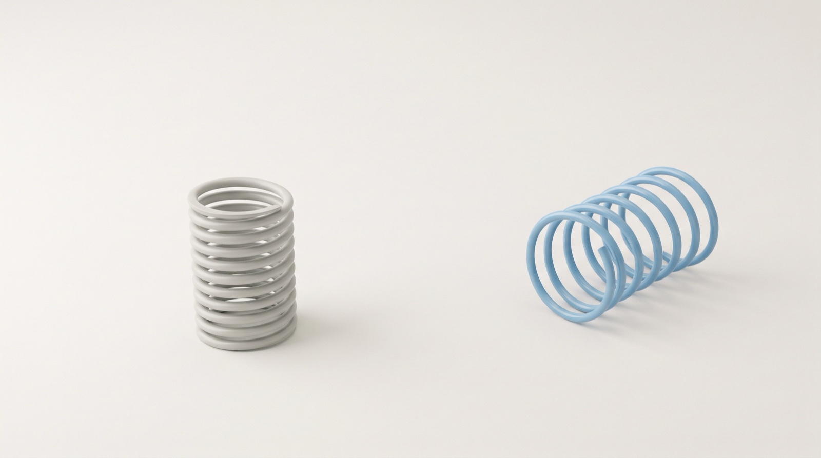 A tightly compressed pale-grey coil standing beside a sky-blue coil resting open at its full relaxed length on a clean off-white surface, like tension that has been let go.