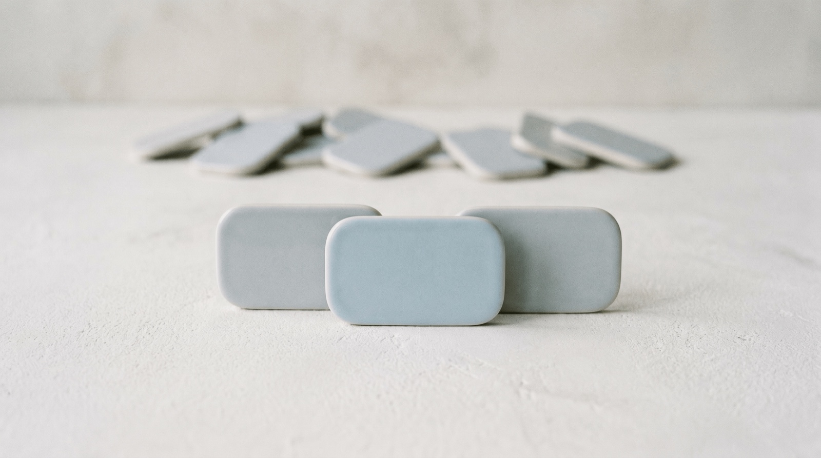A short row of three rounded tiles resting on a soft off-white surface, one in sky-blue lit slightly forward, with a few faint tiles set aside in the background, suggesting a small, calm list of tasks.